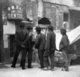 USA: Five Chinese men with queues reading a wall poster, San Francisco Chinatown, c. 1900